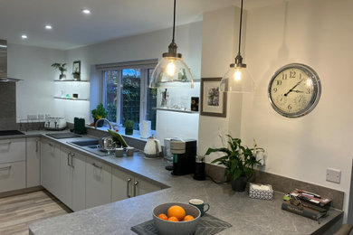 Design ideas for a medium sized modern kitchen in West Midlands with a built-in sink, grey cabinets, grey splashback, black appliances, laminate floors, no island, brown floors, grey worktops and feature lighting.