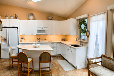 Mid-sized transitional l-shaped medium tone wood floor, brown floor and vaulted ceiling enclosed kitchen photo in DC Metro with a single-bowl sink, flat-panel cabinets, white cabinets, marble countertops, beige backsplash, marble backsplash, white appliances, an island and beige countertops