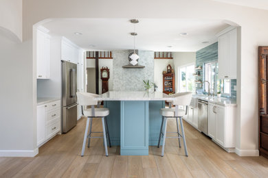Transitional u-shaped light wood floor and beige floor kitchen photo in San Diego with a farmhouse sink, shaker cabinets, white cabinets, blue backsplash, glass tile backsplash, stainless steel appliances, an island and white countertops
