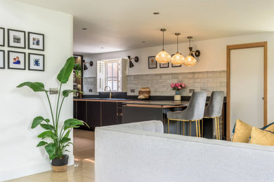 This is an example of a small contemporary l-shaped open plan kitchen in Sussex with an undermount sink, beaded inset cabinets, black cabinets, quartzite benchtops, grey splashback, black appliances, ceramic floors, with island, brown floor and black benchtop.