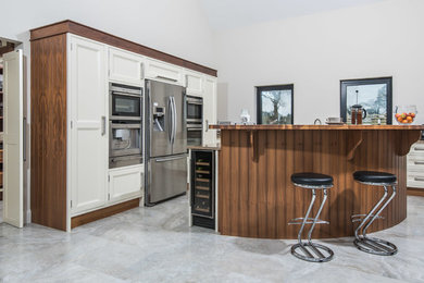 Inspiration for a large contemporary l-shaped open plan kitchen in Belfast with beaded cabinets, white cabinets, granite worktops, stainless steel appliances, an island, multicoloured worktops, a belfast sink, porcelain flooring and white floors.