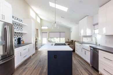 Example of a mid-sized transitional galley dark wood floor, brown floor and vaulted ceiling eat-in kitchen design in Los Angeles with a drop-in sink, shaker cabinets, white cabinets, marble countertops, white backsplash, subway tile backsplash, stainless steel appliances, an island and black countertops