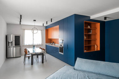 Immagine di una grande cucina minimal con ante blu, top in marmo, paraspruzzi arancione, paraspruzzi in marmo, elettrodomestici in acciaio inossidabile, pavimento in cemento, pavimento grigio e top bianco
