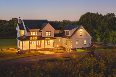 Foto della villa grande bianca country a due piani con rivestimenti misti, tetto a capanna, copertura mista, tetto nero e pannelli e listelle di legno