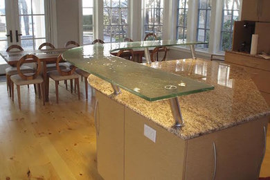 Example of a mid-sized trendy l-shaped light wood floor eat-in kitchen design in Denver with flat-panel cabinets, light wood cabinets, glass countertops, an island and stainless steel appliances