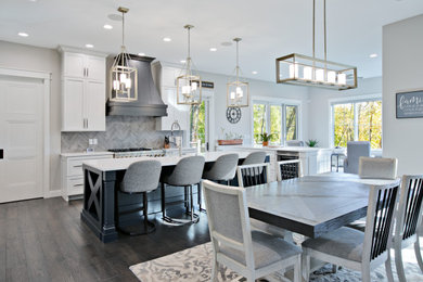 Photo of a large transitional eat-in kitchen in Other with a farmhouse sink, shaker cabinets, white cabinets, quartzite benchtops, grey splashback, porcelain splashback, stainless steel appliances, dark hardwood floors, multiple islands, brown floor and white benchtop.