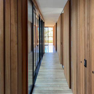 Cette photo montre un couloir tendance de taille moyenne avec un mur marron, un sol en bois clair, un sol marron, un plafond en lambris de bois et boiseries.