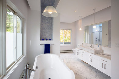 Photo of a large midcentury master bathroom in Boston with flat-panel cabinets, white cabinets, a freestanding tub, an alcove shower, a two-piece toilet, blue tile, white tile, mosaic tile, white walls, marble floors, a trough sink and marble benchtops.