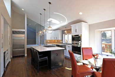 Example of a large transitional u-shaped dark wood floor and brown floor eat-in kitchen design in St Louis with shaker cabinets, white cabinets, quartz countertops, an island, white countertops, a farmhouse sink, gray backsplash, subway tile backsplash and stainless steel appliances