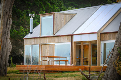 Small beach style split-level grey house exterior in Napier-Hastings with wood siding, a gable roof and a metal roof.