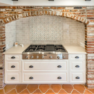 Свежая идея для дизайна: большая параллельная кухня в средиземноморском стиле с кладовкой, раковиной в стиле кантри, фасадами с выступающей филенкой, белыми фасадами, столешницей из кварцевого композита, разноцветным фартуком, фартуком из керамогранитной плитки, техникой из нержавеющей стали, полом из терракотовой плитки, островом и оранжевым полом - отличное фото интерьера