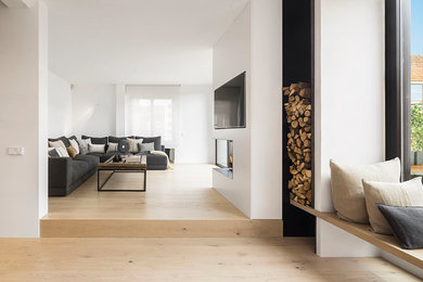 Inspiration for a large contemporary open concept family room in Barcelona with white walls, medium hardwood floors, a corner fireplace, a concrete fireplace surround and a wall-mounted tv.