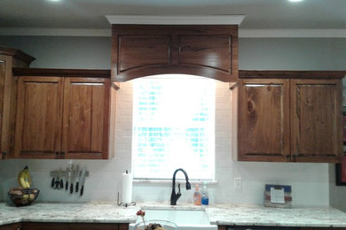 Mid-sized trendy l-shaped porcelain tile and gray floor eat-in kitchen photo in New Orleans with a farmhouse sink, raised-panel cabinets, brown cabinets, granite countertops, white backsplash, ceramic backsplash, stainless steel appliances and an island
