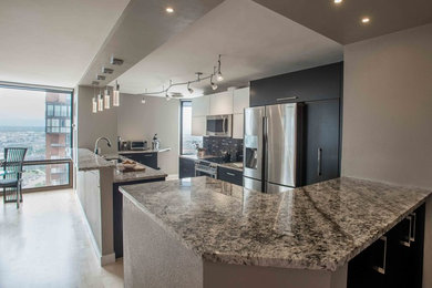 Open concept kitchen - small modern galley light wood floor open concept kitchen idea in Denver with an undermount sink, flat-panel cabinets, black cabinets, granite countertops, black backsplash, glass tile backsplash, stainless steel appliances and a peninsula