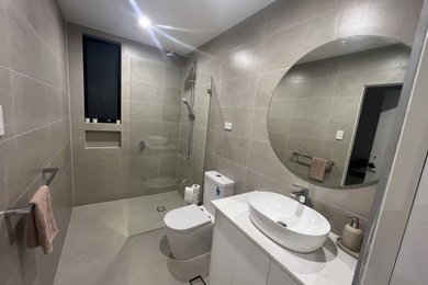 This is an example of a mid-sized modern master bathroom in Sydney with beaded inset cabinets, white cabinets, an open shower, a one-piece toilet, beige tile, ceramic tile, beige walls, ceramic floors, a vessel sink, quartzite benchtops, beige floor, an open shower, white benchtops, a single vanity, a freestanding vanity and recessed.
