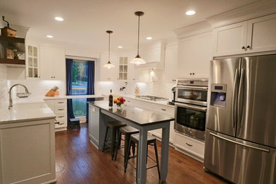 Mid-sized transitional u-shaped medium tone wood floor and brown floor kitchen photo in Louisville with a farmhouse sink, shaker cabinets, white cabinets, white backsplash, subway tile backsplash, stainless steel appliances, an island, quartz countertops and white countertops