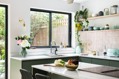 This is an example of a medium sized eclectic u-shaped kitchen/diner in London with an integrated sink, flat-panel cabinets, green cabinets, quartz worktops, cement tile splashback, integrated appliances, light hardwood flooring, an island, beige floors, white worktops and a feature wall.