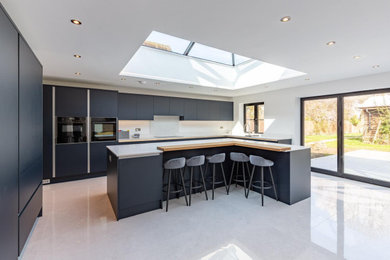 Large contemporary u-shaped open plan kitchen in Other with a submerged sink, flat-panel cabinets, blue cabinets, quartz worktops, white splashback, black appliances, an island, grey floors, white worktops and a vaulted ceiling.