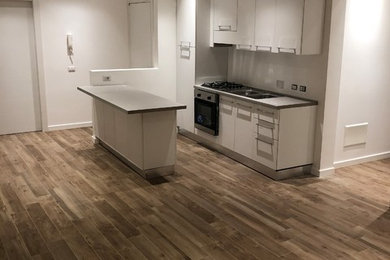 Ispirazione per una piccola cucina abitabile scandinava con ante lisce, ante bianche, penisola, lavello da incasso, elettrodomestici in acciaio inossidabile, pavimento in gres porcellanato e pavimento marrone