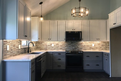 Large transitional u-shaped eat-in kitchen in Kansas City with an undermount sink, recessed-panel cabinets, grey cabinets, quartzite benchtops, green splashback, mosaic tile splashback, black appliances, laminate floors, no island, brown floor and white benchtop.