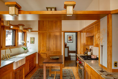 Arts and crafts u-shaped kitchen in Minneapolis with a farmhouse sink, shaker cabinets, medium wood cabinets, white splashback, subway tile splashback, panelled appliances, medium hardwood floors, with island, brown floor, grey benchtop and vaulted.