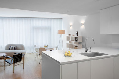 Example of a mid-sized trendy light wood floor eat-in kitchen design in New York with an undermount sink, flat-panel cabinets, white cabinets, quartz countertops, white backsplash and a peninsula