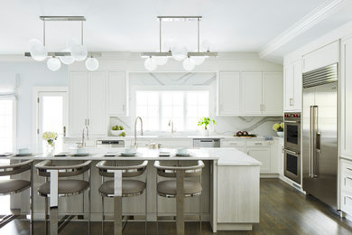 Example of a large transitional l-shaped medium tone wood floor and brown floor enclosed kitchen design in New York with an undermount sink, recessed-panel cabinets, white cabinets, white backsplash, stainless steel appliances, an island and white countertops