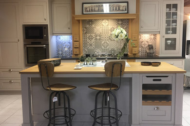 Large transitional galley open plan kitchen in Le Havre with a double-bowl sink, louvered cabinets, grey cabinets, wood benchtops, grey splashback, cement tile splashback, panelled appliances, ceramic floors, with island and white floor.