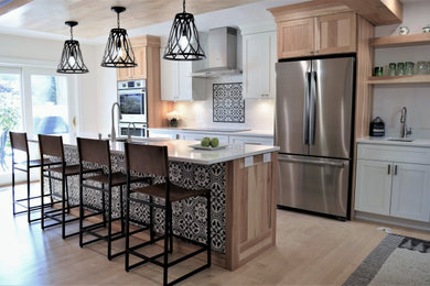 Example of a mid-sized country single-wall light wood floor, beige floor and wood ceiling open concept kitchen design in New York with a single-bowl sink, shaker cabinets, light wood cabinets, quartzite countertops, black backsplash, ceramic backsplash, stainless steel appliances, an island and white countertops
