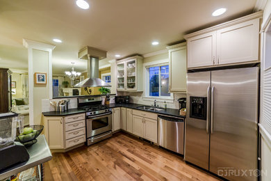 This is an example of a traditional kitchen in Seattle with shaker cabinets, white cabinets, no island, a double-bowl sink, granite benchtops, white splashback, ceramic splashback, stainless steel appliances, laminate floors and brown floor.
