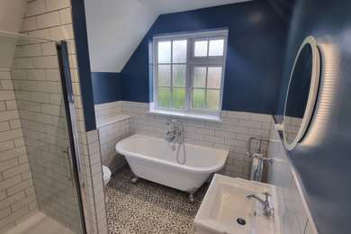 This is an example of a medium sized traditional family bathroom in West Midlands with shaker cabinets, white cabinets, a freestanding bath, an alcove shower, a one-piece toilet, white tiles, ceramic tiles, blue walls, porcelain flooring, multi-coloured floors, a hinged door, a wall niche, a single sink and a freestanding vanity unit.