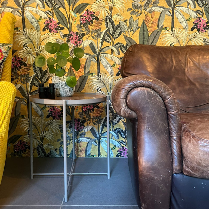 This room blends eclectic charm with a cozy, lived-in warmth. A bold botanical feature wall sets the tone, creating a lush backdrop for the rich, weathered leather sofa and the mix of vintage wooden p