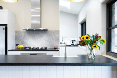 This is an example of a modern open plan kitchen in Sydney with a farmhouse sink, white cabinets, grey splashback, stone slab splashback, with island, brown floor and black benchtop.