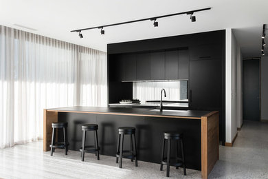 Photo of a contemporary galley kitchen in Hobart with a farmhouse sink, flat-panel cabinets, black cabinets, panelled appliances, concrete floors, with island, grey floor and black benchtop.