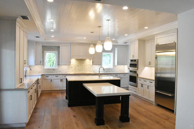 Example of a large transitional u-shaped medium tone wood floor and brown floor kitchen design in Tampa with a farmhouse sink, white cabinets, quartz countertops, green backsplash, ceramic backsplash, stainless steel appliances and an island