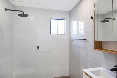 This is an example of a small contemporary bathroom in Newcastle - Maitland with furniture-like cabinets, white cabinets, an open shower, a wall-mount toilet, white tile, ceramic tile, white walls, ceramic floors, a wall-mount sink, solid surface benchtops, grey floor, an open shower and white benchtops.