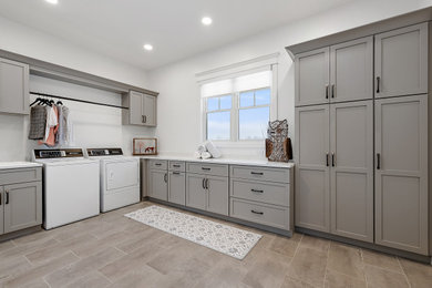 Example of a large transitional l-shaped porcelain tile and gray floor dedicated laundry room design in Detroit with shaker cabinets, gray cabinets, quartz countertops, white backsplash, quartz backsplash, white walls, a side-by-side washer/dryer, white countertops and a drop-in sink