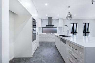 Large modern l-shaped open plan kitchen in Melbourne with a double-bowl sink, white cabinets, marble benchtops, grey splashback, ceramic splashback, panelled appliances, porcelain floors, with island, grey floor and white benchtop.