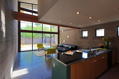Inspiration for a mid-sized modern galley open plan kitchen in Phoenix with a double-bowl sink, flat-panel cabinets, medium wood cabinets, granite benchtops, black appliances and concrete floors.