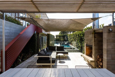 This is an example of a contemporary backyard deck in Auckland with with fireplace and a pergola.