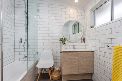 Photo of a contemporary bathroom in Brisbane with flat-panel cabinets, light wood cabinets, an alcove tub, a shower/bathtub combo, white tile, subway tile, white walls and a console sink.