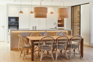 Ejemplo de cocina comedor alargada y blanca y madera clásica renovada grande con fregadero bajoencimera, armarios con paneles empotrados, puertas de armario blancas, encimera de cuarzo compacto, electrodomésticos negros, suelo laminado, una isla, suelo marrón, encimeras beige y barras de cocina