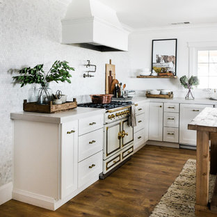 Photo of a mid-sized country u-shaped kitchen in Other with a farmhouse sink, shaker cabinets, white cabinets, concrete benchtops, white splashback, marble splashback, white appliances, laminate floors, with island and white benchtop.