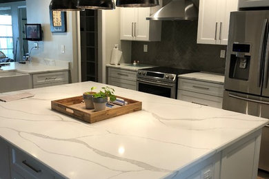 Large country l-shaped dark wood floor and brown floor eat-in kitchen photo in Tampa with a farmhouse sink, recessed-panel cabinets, white cabinets, quartzite countertops, gray backsplash, ceramic backsplash, stainless steel appliances, an island and white countertops