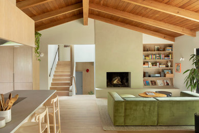 Inspiration for a mid-sized 1950s open concept light wood floor, brown floor and exposed beam living room library remodel in Portland with beige walls, a standard fireplace, a plaster fireplace and no tv
