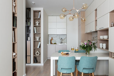 This is an example of a small contemporary l-shaped eat-in kitchen in Saint Petersburg with an undermount sink, flat-panel cabinets, beige cabinets, solid surface benchtops, white splashback, porcelain splashback, white appliances, porcelain floors, no island, beige floor and white benchtop.