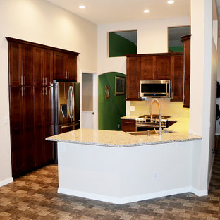 Mid-sized contemporary kitchen pantry inspiration - Mid-sized trendy u-shaped porcelain floor kitchen pantry photo in Tampa with a farmhouse sink, shaker cabinets, brown cabinets, granite countertops, beige backsplash, glass tile backsplash, stainless steel appliances and a peninsula