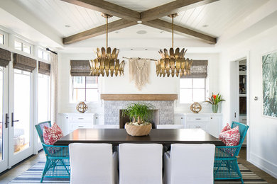 Inspiration for a large tropical dining room in Orange County with white walls, medium hardwood floors, a standard fireplace, a stone fireplace surround and brown floor.