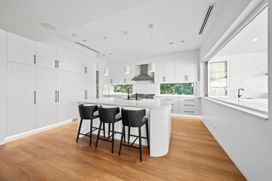 This is an example of a large l-shaped open plan kitchen in Sydney with an undermount sink, shaker cabinets, white cabinets, quartz benchtops, white splashback, engineered quartz splashback, stainless steel appliances, laminate floors, with island, yellow floor and white benchtop.