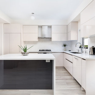 This is an example of a large modern l-shaped open plan kitchen in Toronto with an undermount sink, flat-panel cabinets, beige cabinets, quartz benchtops, white splashback, engineered quartz splashback, stainless steel appliances, light hardwood floors, with island, beige floor, white benchtop and wallpaper.